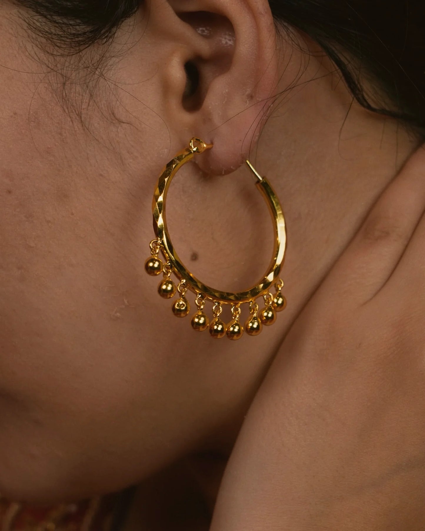 Gold hoop earring with dangling beads worn by a person.