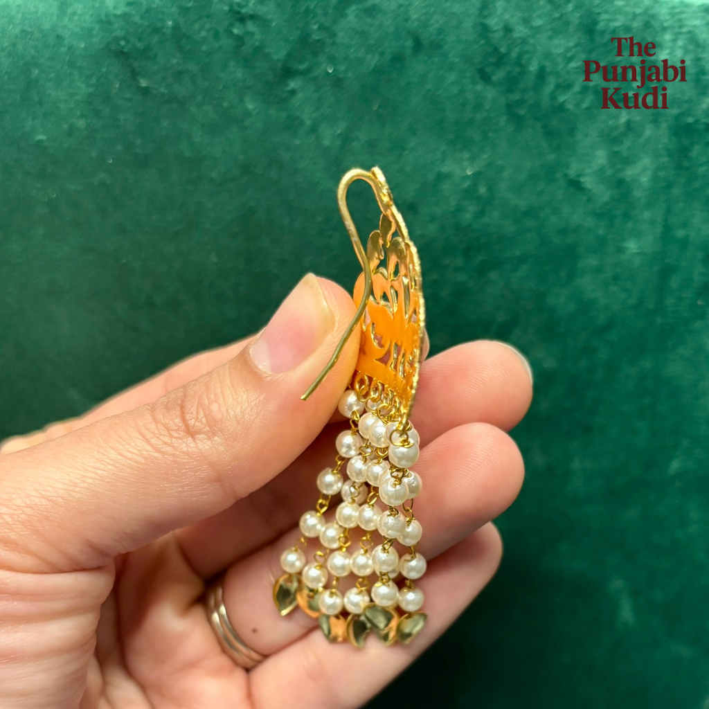 Gold and pearl earring held in a hand against a green background with 'The Punjabi Kudi' branding.
